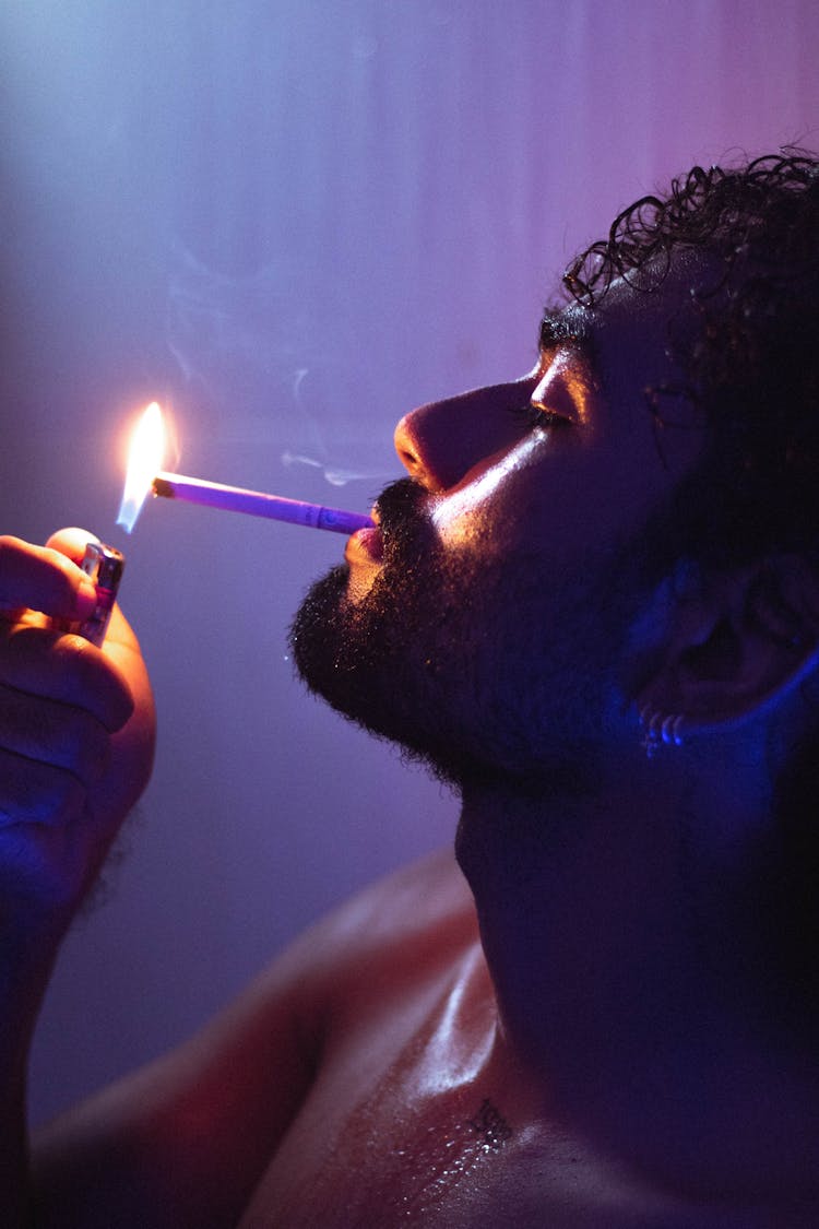 Close-up Of Man Lighting Cigarette In Neon Lights
