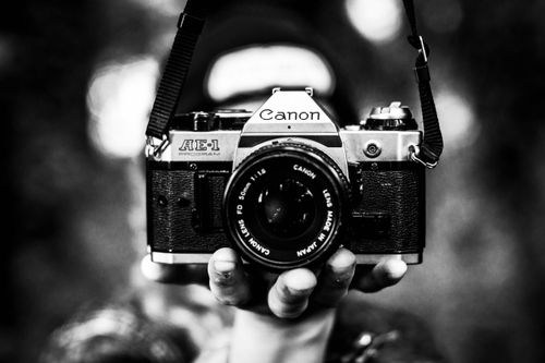 Free Close-up of a vintage Canon AE-1 camera held in hand, captured in black and white. Stock Photo