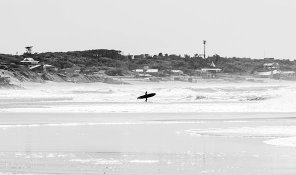 Silhouette of a surfer walking along an empty beach in black and white.