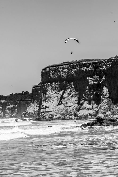 Free A paraglider soars above rugged coastal cliffs by the ocean. Stock Photo