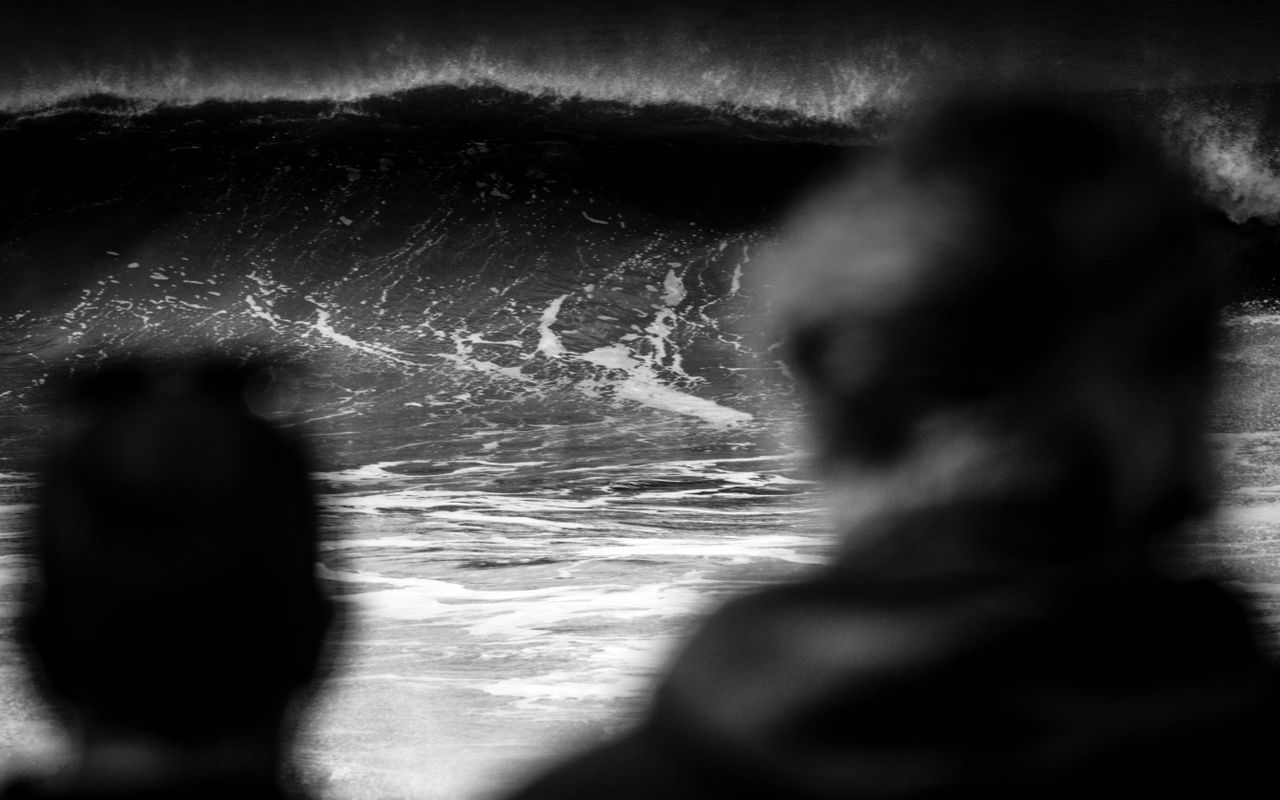 black and white photo of ocean waves with silhouetted figures in foreg