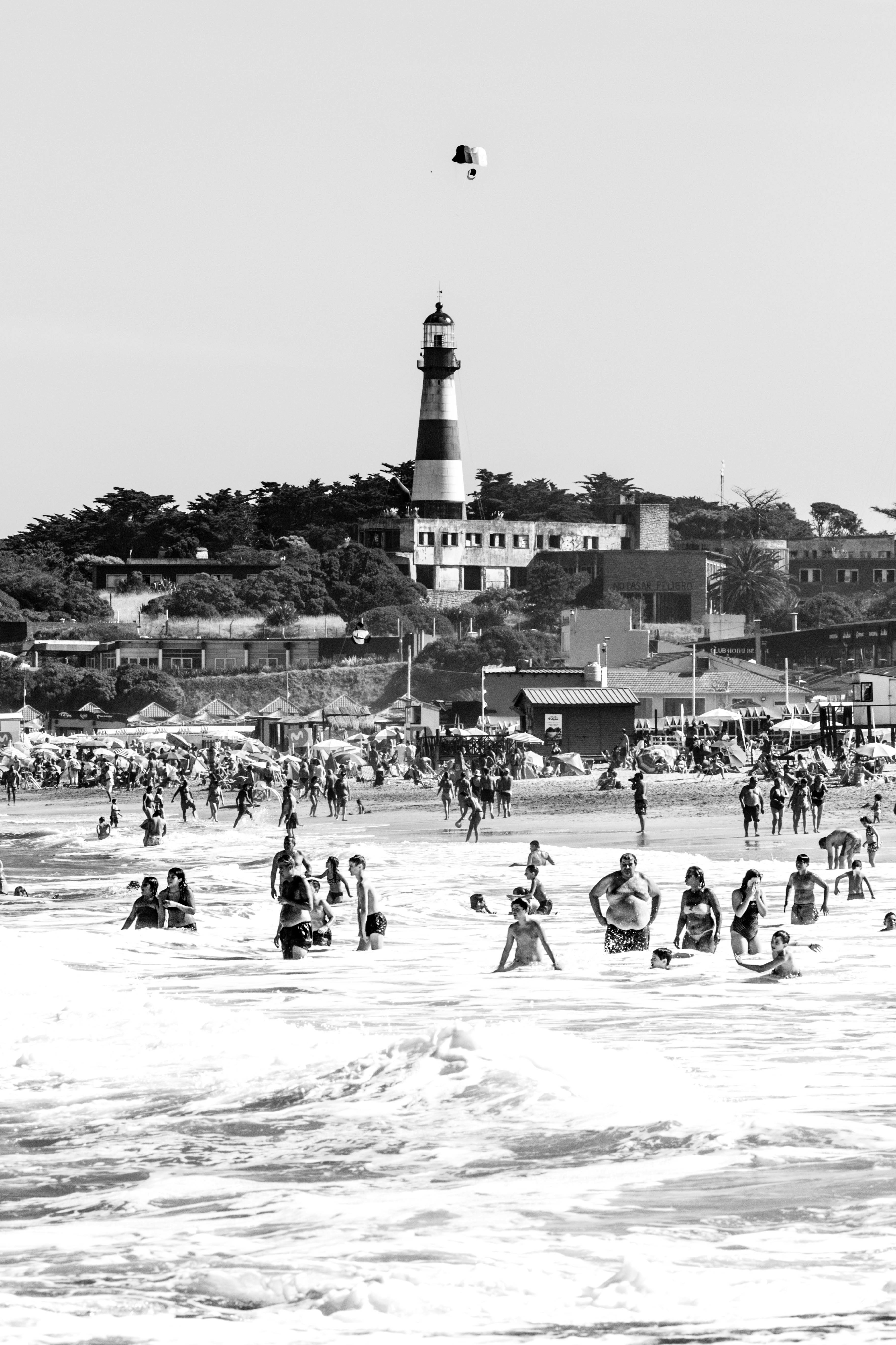 Black and white image of a bustling beach scene with a lighthouse and parachute.