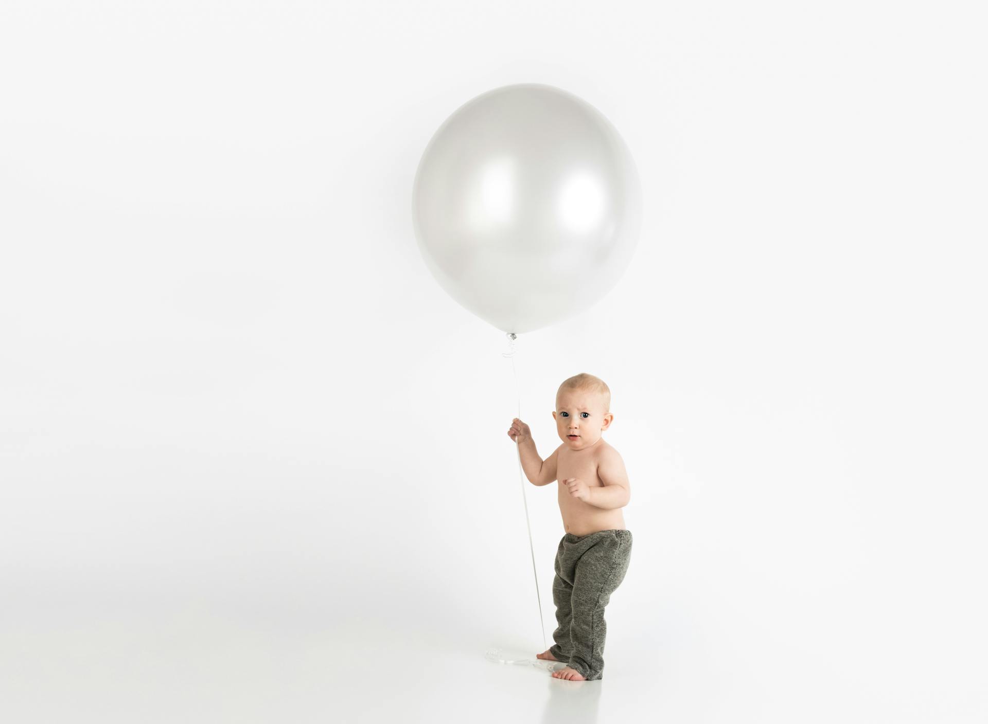 Cute baby holding a large balloon in a clean, minimalist studio setup. Perfect for child-focused advertising.