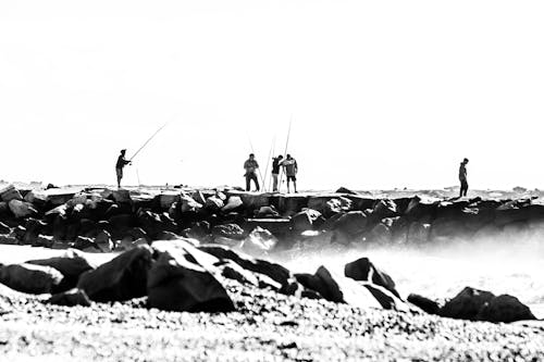 Grayscale Photo of Men Fishing on the Seawall