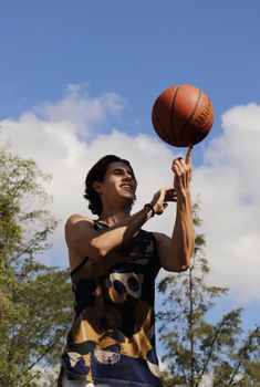A young man skillfully spins a basketball on his finger under a blue sky.