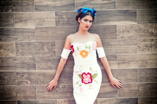 Stylish woman posing in an elegant floral dress against a wooden wall.