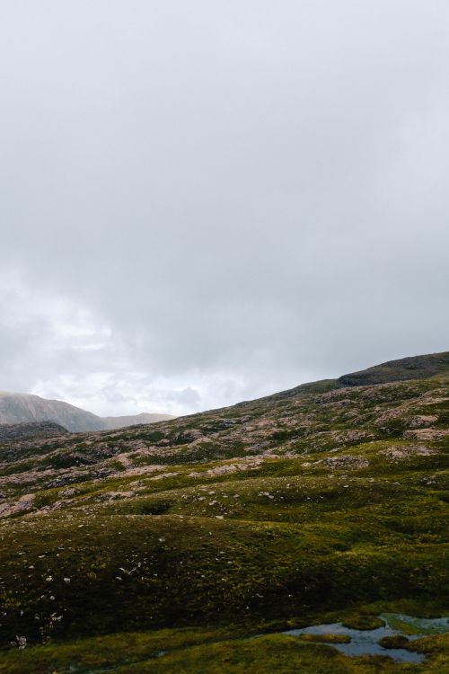 Free A scenic landscape of rolling hills under a dramatic overcast sky, perfect for nature backgrounds. Stock Photo