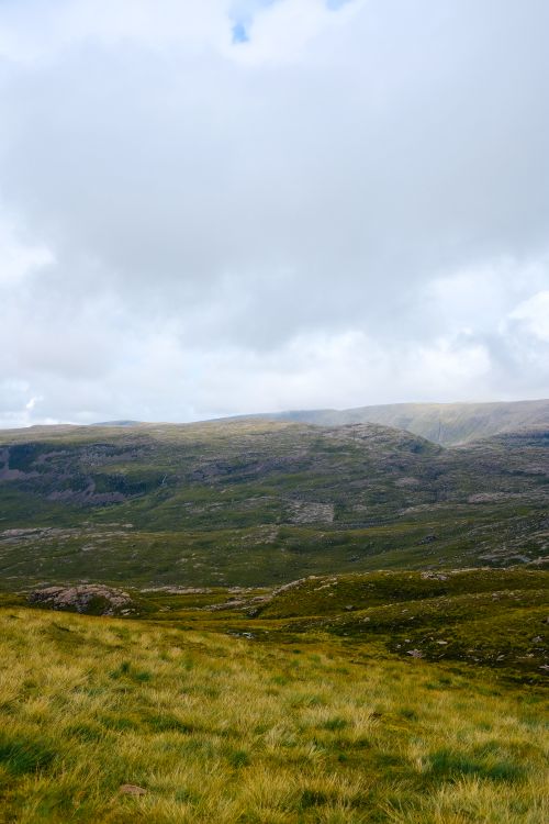 Free A breathtaking aerial view of lush green grasslands and hills beneath a cloudy sky. Stock Photo