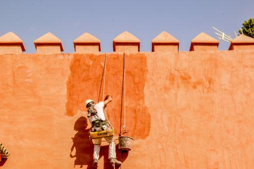 Free A worker repaints an orange brick wall in the sun, using ropes for support. Stock Photo
