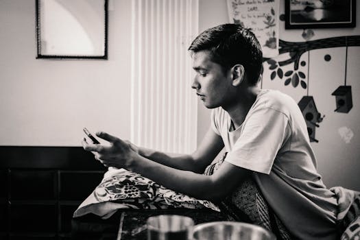 Black and white photo of a young man texting on a mobile device indoors.