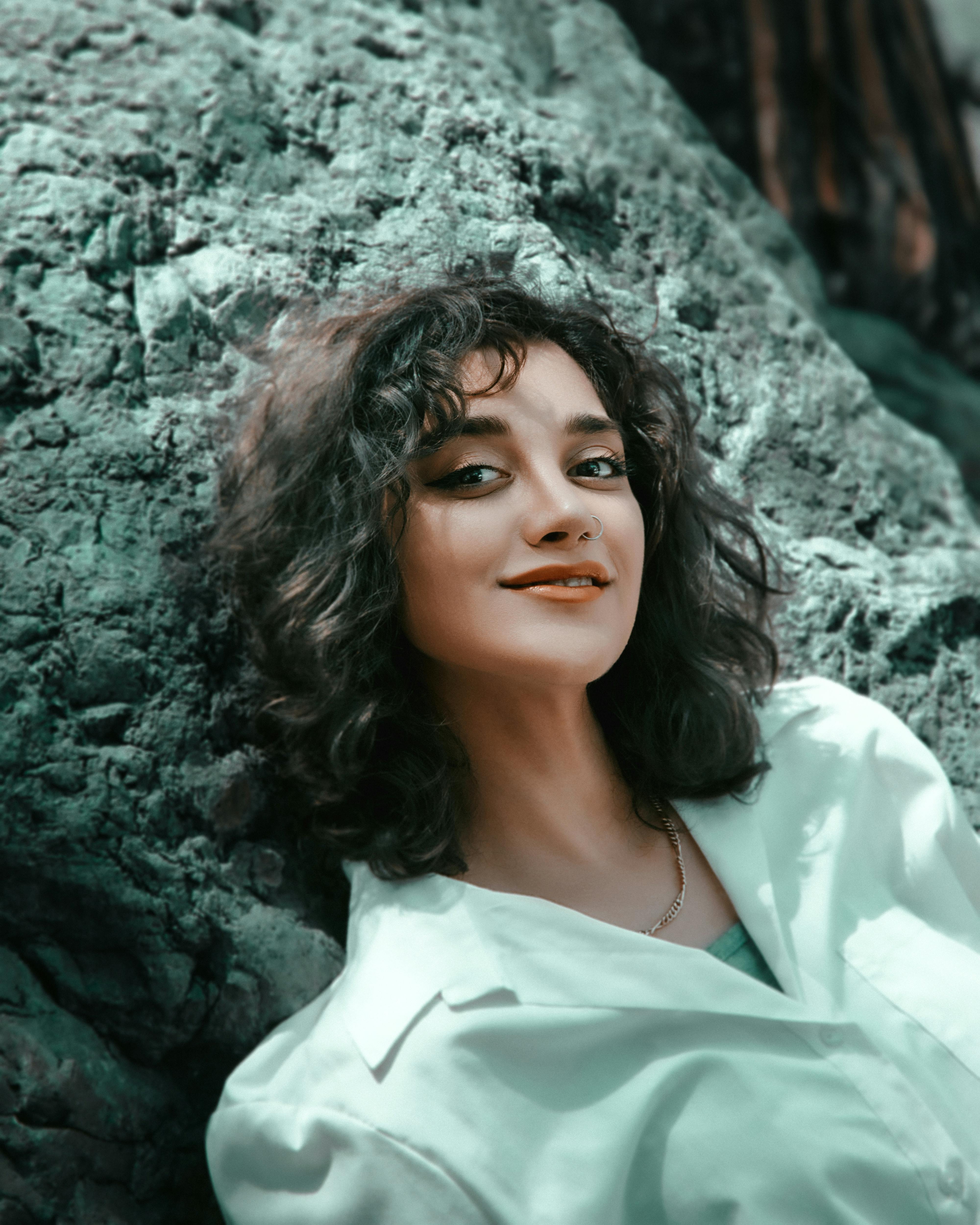 A smiling woman with curly hair enjoying a sunny day outdoors against a rocky backdrop.