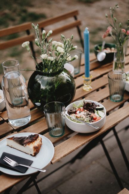 A beautiful outdoor dining setup featuring a fresh salad, dessert, and floral decoration on a wooden table.