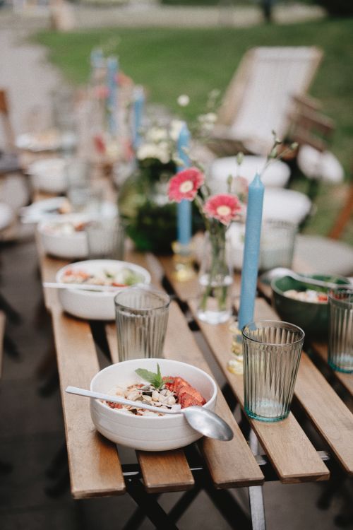 Free Stylish outdoor brunch setting with fresh food bowls, flowers, and candles on wooden table. Stock Photo