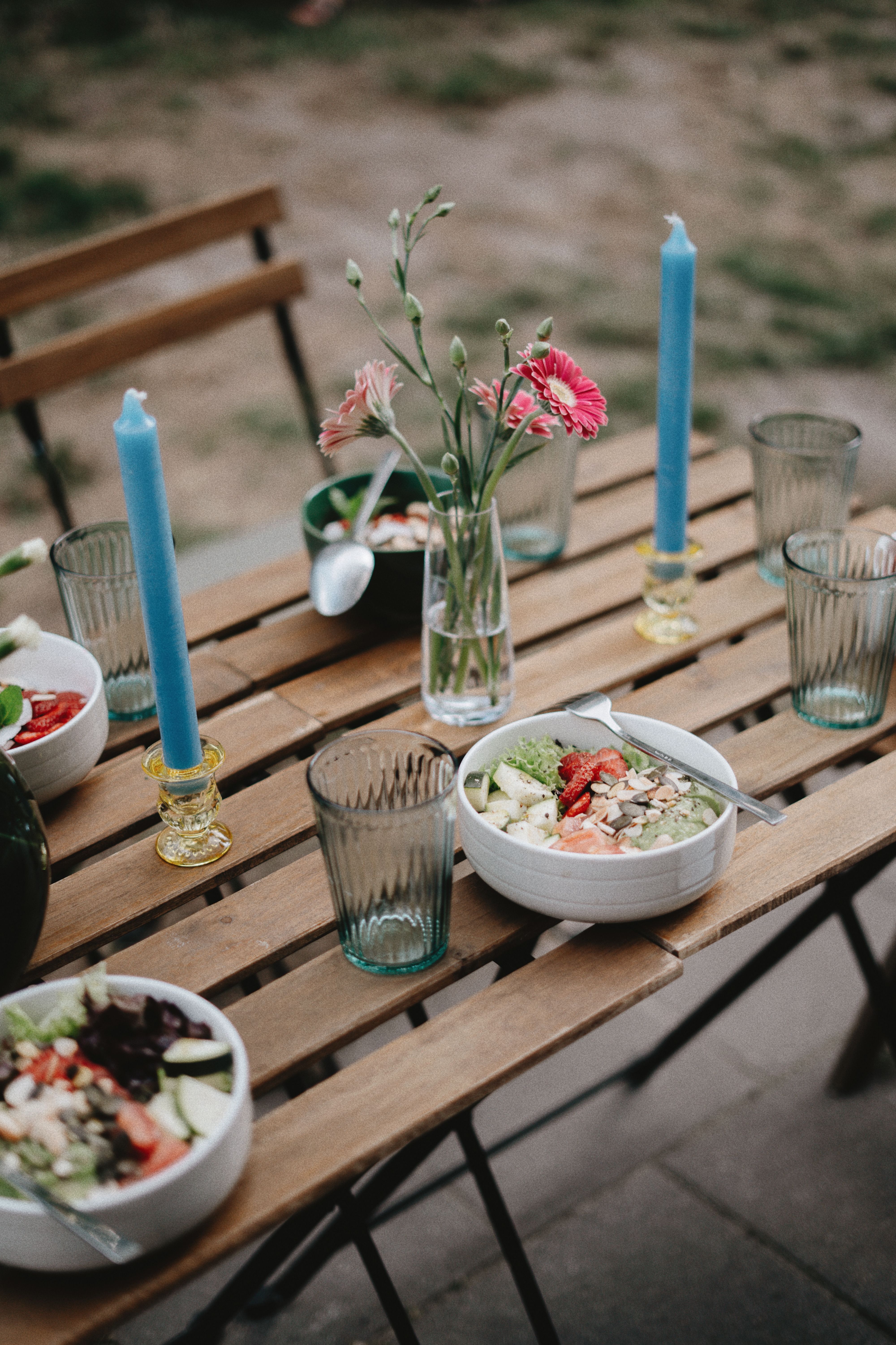 A beautifully set outdoor table with healthy salads, candles, and flowers creating a serene dining atmosphere.