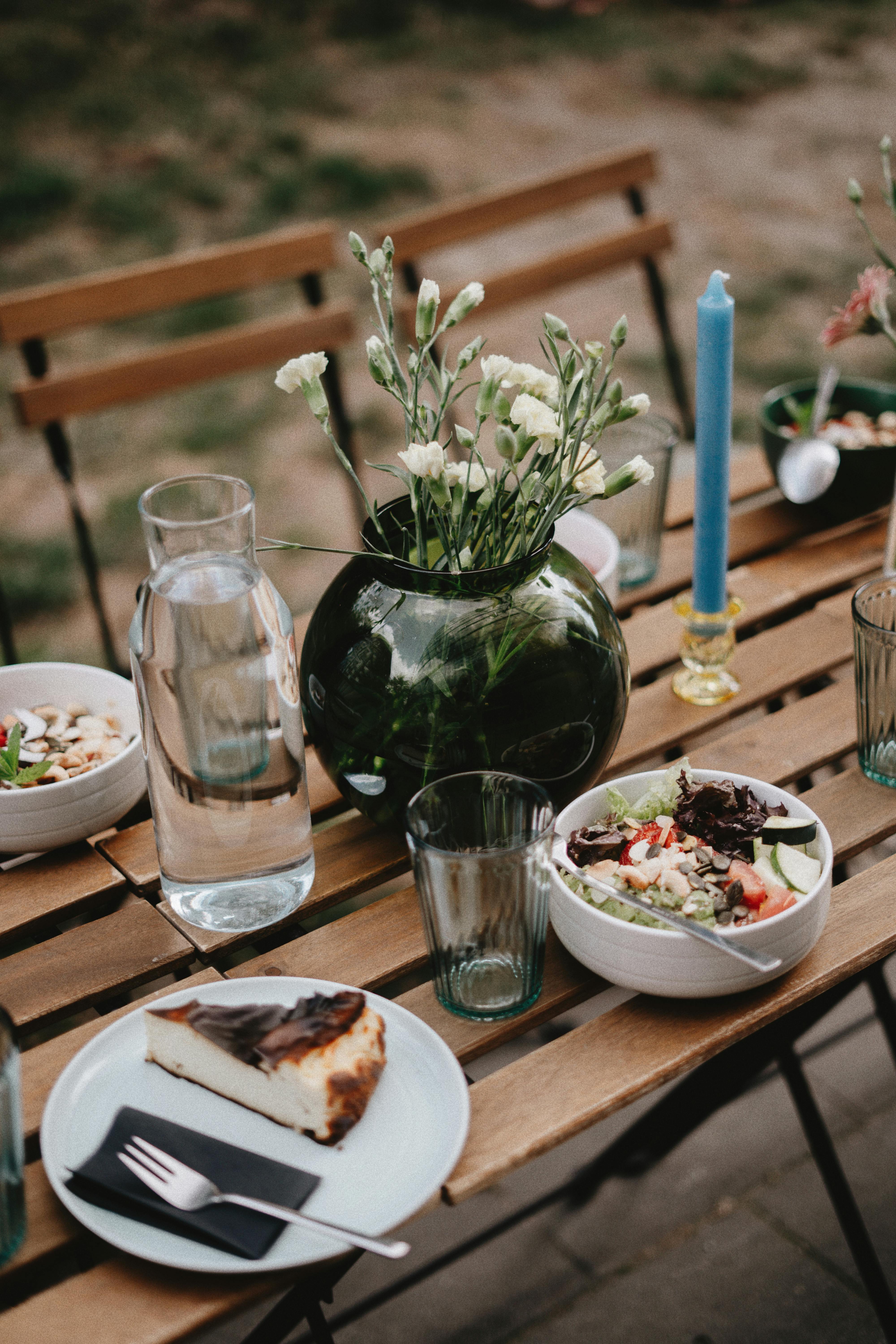 A beautifully arranged outdoor table setting with fresh salad, cake, and elegant decor.