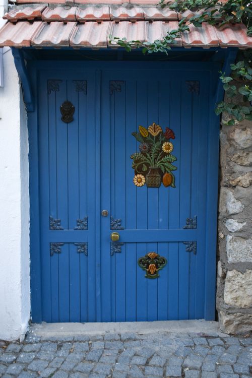 Free Vibrant blue door adorned with floral motifs set in a rustic stone wall, providing an artistic exterior scene. Stock Photo