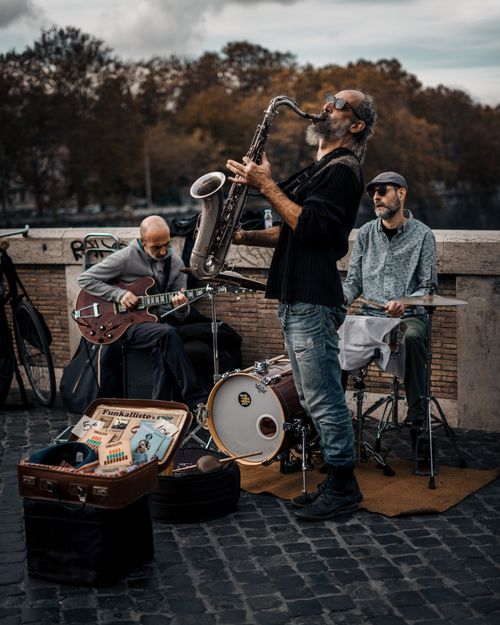 Free Live street performance by musicians in Rome, featuring saxophone, guitar, and drums. Stock Photo