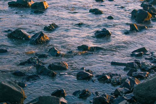 Free A serene rocky shoreline with gentle waves at sunset, creating a tranquil ambiance. Stock Photo