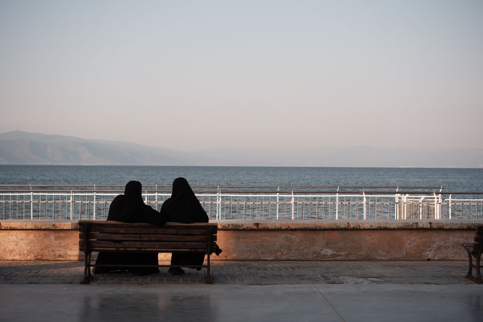 Two women in traditional clothing sit by the sea, enjoying a peaceful moment.