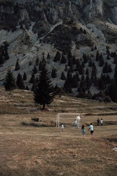 Group of children playing soccer on grassy field against mountain backdrop.