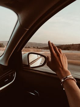 A hand with bracelets reaches out from a car window, depicting freedom and travel.