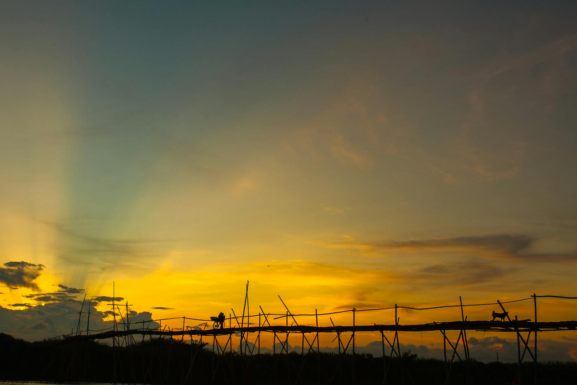 Silhouette of people and a dog on a wooden bridge at sunset, under a vibrant, colorful sky.