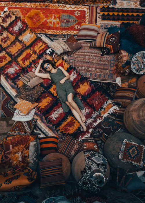 Free A woman in a green dress lies on colorful traditional rugs with ethnic patterns, creating a cozy market vibe. Stock Photo