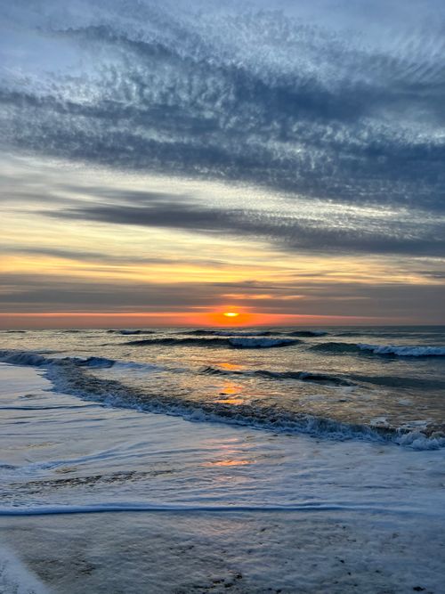 Free A breathtaking sunrise over a tranquil beach, with waves gently lapping the shore under a dramatic sky. Stock Photo