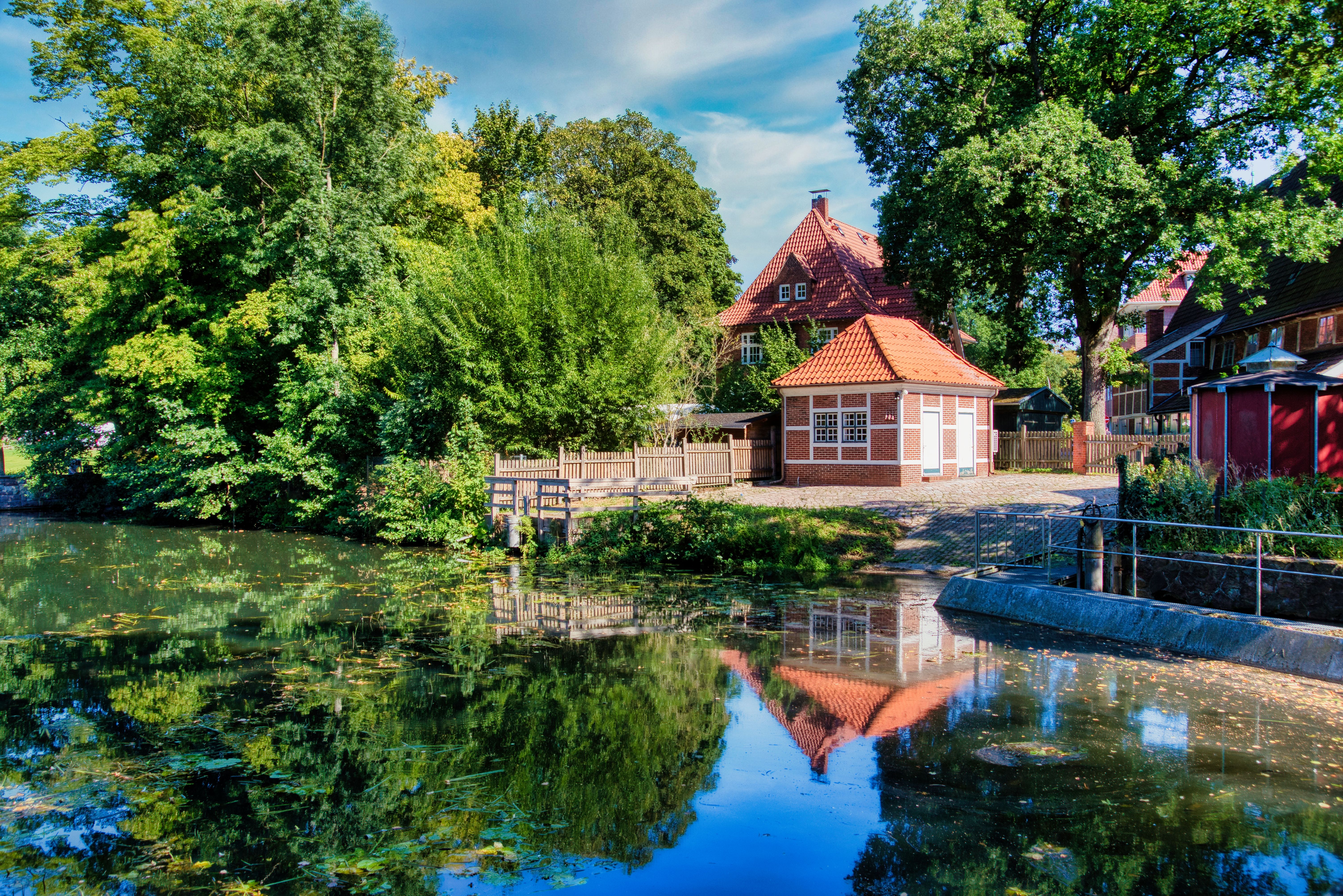 Picturesque countryside view with cottage, trees, and serene lake reflection.