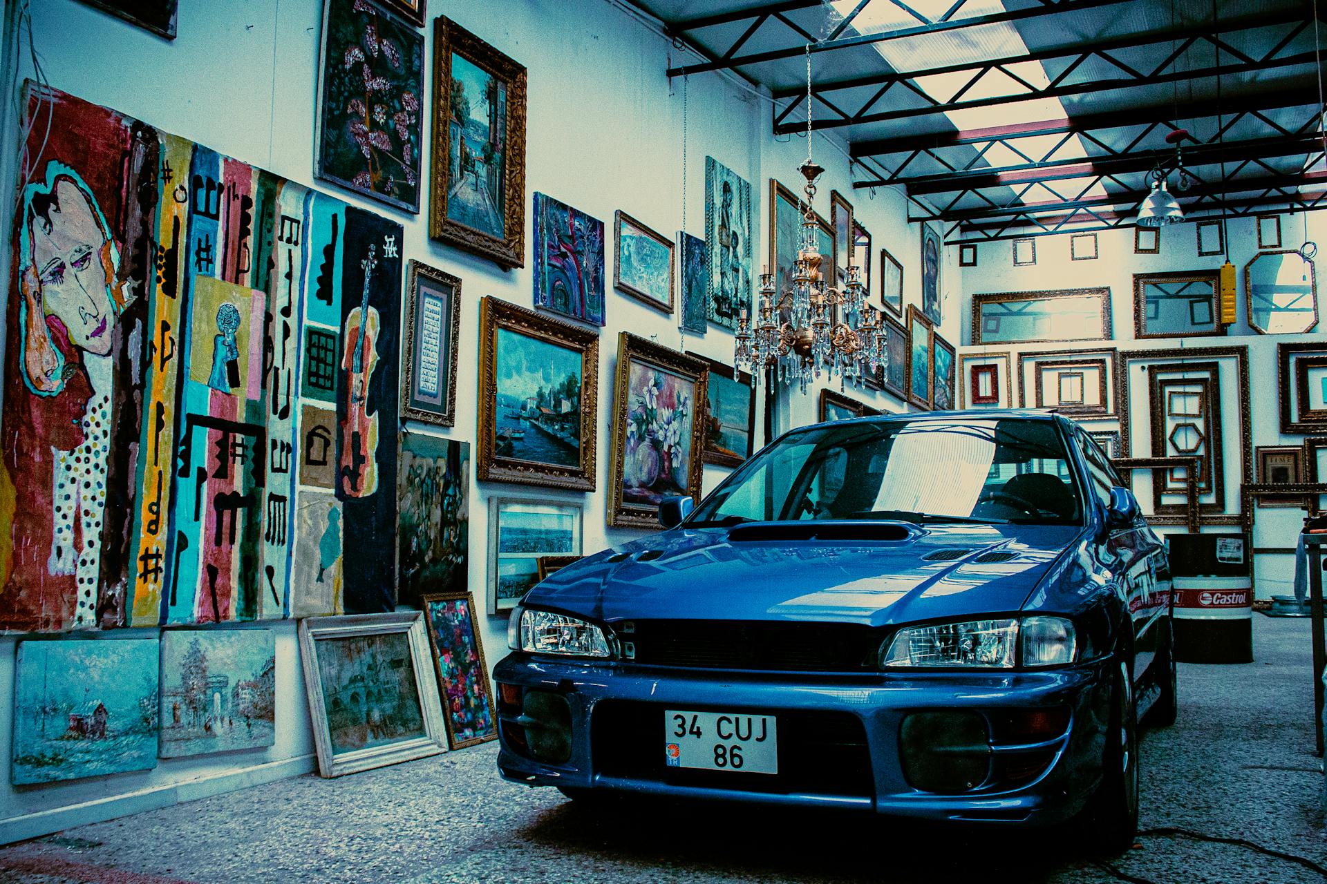 A blue Subaru parked inside a vibrant art gallery with multiple paintings on display.