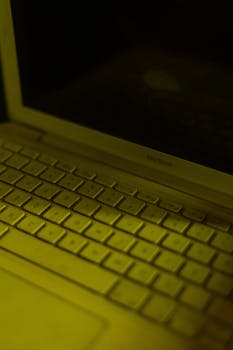 Close-up of a MacBook keyboard in low light with a yellow tint, captured indoors.