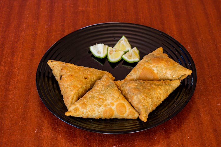 Samosas And Lime Slices On Black Plate