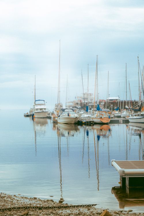 Free Peaceful harbor scene with yachts and reflections in calm water under a blue sky at dawn. Stock Photo