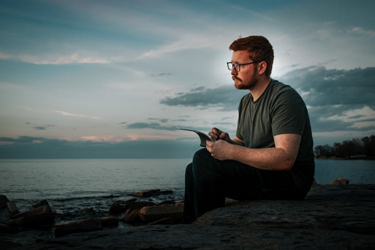 Man In Gray Shirt Sitting On A Rock Looking Afar On The Sea