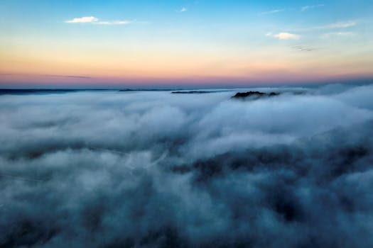 Stunning aerial view of a misty landscape enveloped in clouds at sunset, creating a serene scene.