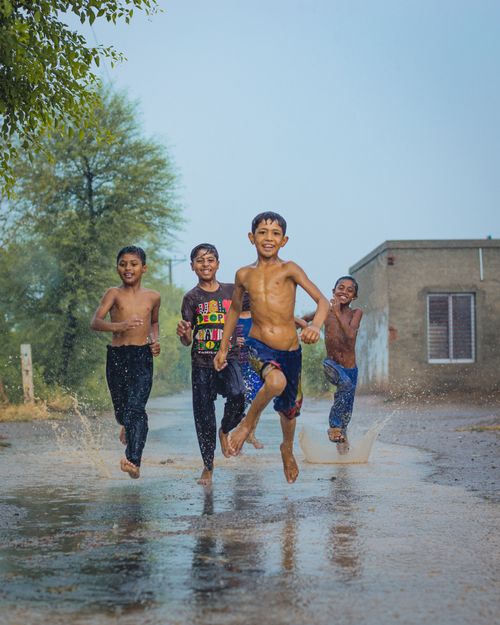 Free Four happy boys playing in rain puddles, Sargodha, capturing the essence of childhood fun. Stock Photo