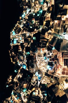 Stunning aerial view of Santorini at night, highlighting illuminated rooftops and pools.