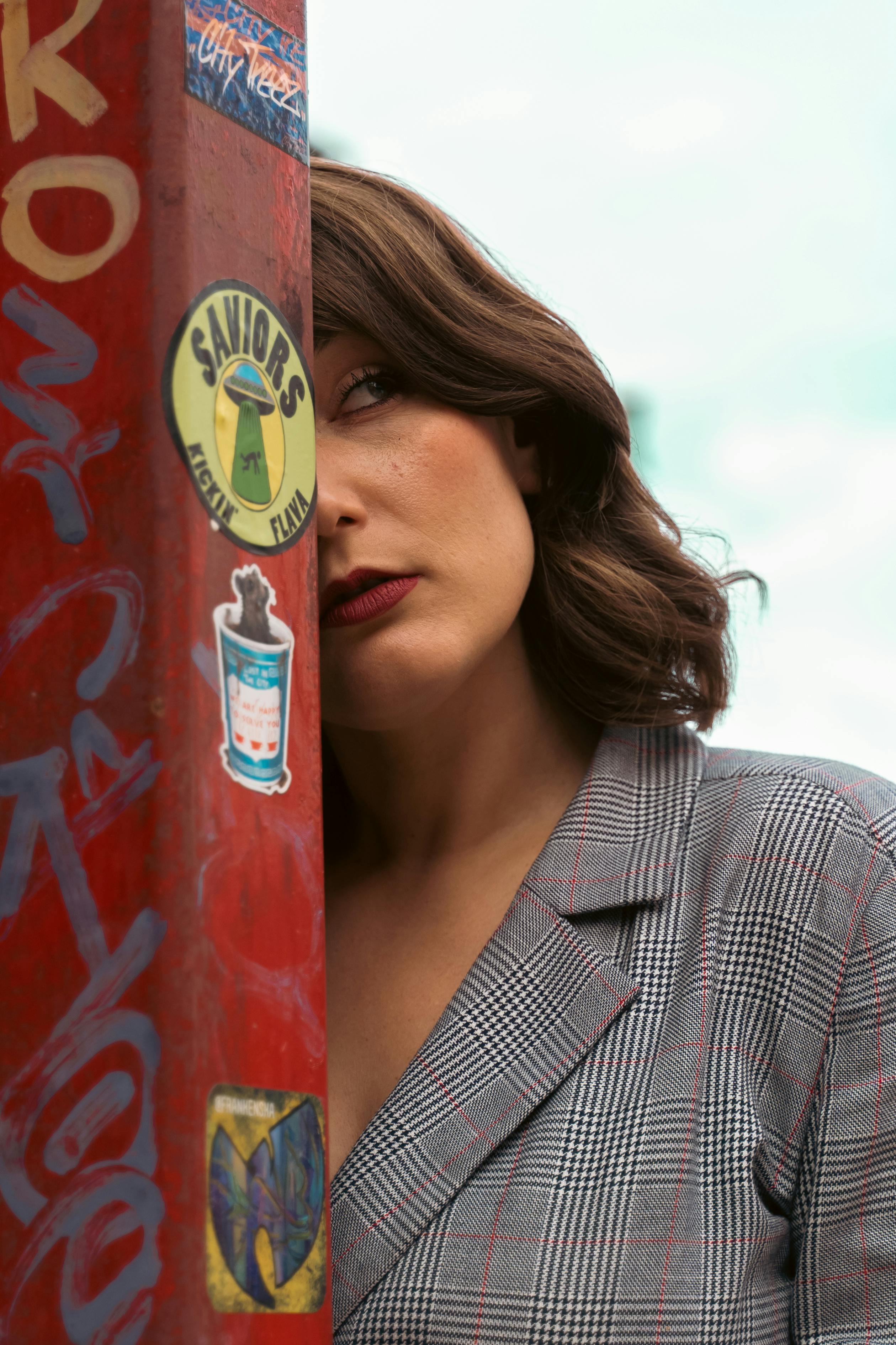 Captivating portrait of a woman posing by a graffiti-covered pole in an urban setting.