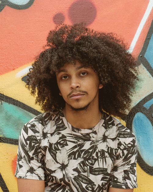 Free Young man with afro hair posing against a colorful graffiti wall for a portrait. Stock Photo