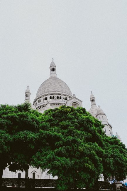Beautiful view of Sacre Coeur Basilica's domes with lush greenery, capturing an overcast sky.