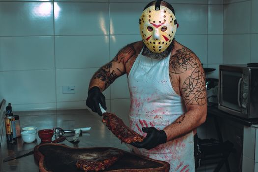 A masked man in a bloody apron prepares ribs in a kitchen. Perfect for Halloween or horror themes.