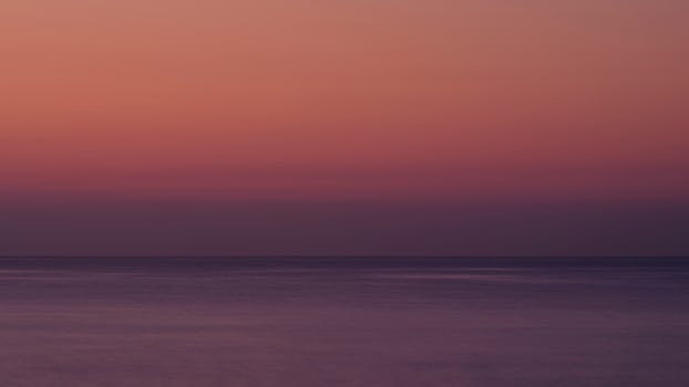 A serene sunset over the calm ocean with a gradient sky of warm colors.