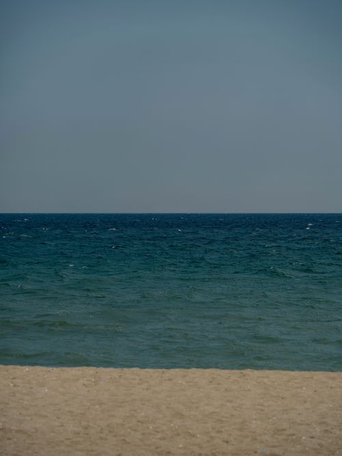 Free Serene view of a sandy beach and calm ocean waves under a clear blue sky. Stock Photo