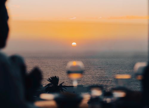 Free Explore a tranquil ocean sunset with silhouettes and blurred foreground, perfect for serene moments. Stock Photo