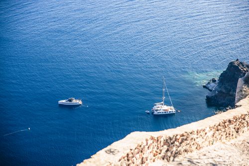 Free Aerial view of two yachts anchored near a rocky coastline in clear blue waters. Stock Photo