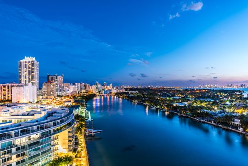 Free Stunning aerial view of Miami's illuminated waterfront skyline during dusk showcasing modern architecture and vibrant city lights. Stock Photo