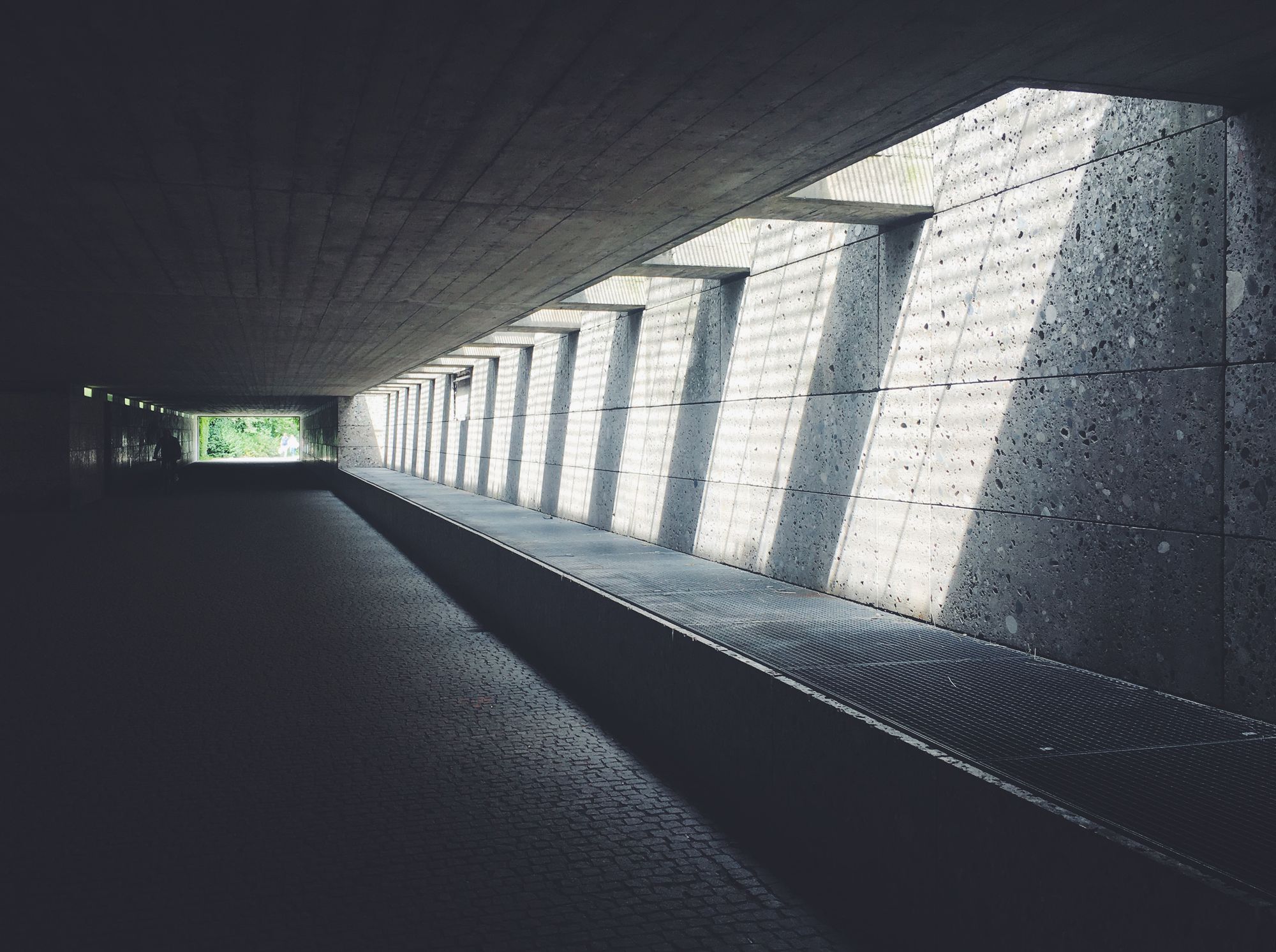 Concrete colonnade with deep shadow and shafts of daylight along a long passage