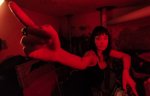 Free A bold image of a woman with tattoos pointing in a red-lit room, creating a dramatic atmosphere. Stock Photo