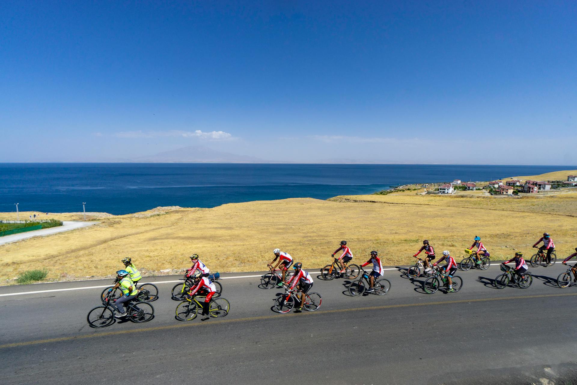 Cyclists compete along a scenic coastal road with ocean views under a clear blue sky.