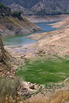 Tranquil natural landscape of Iznájar Reservoir, showcasing arid cliffs and green terrain.